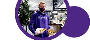 Masked student in a Western hoodie holding food from dining hall