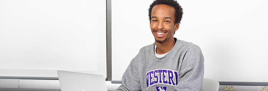 Student wearing Western sweatshirt sitting with a laptop