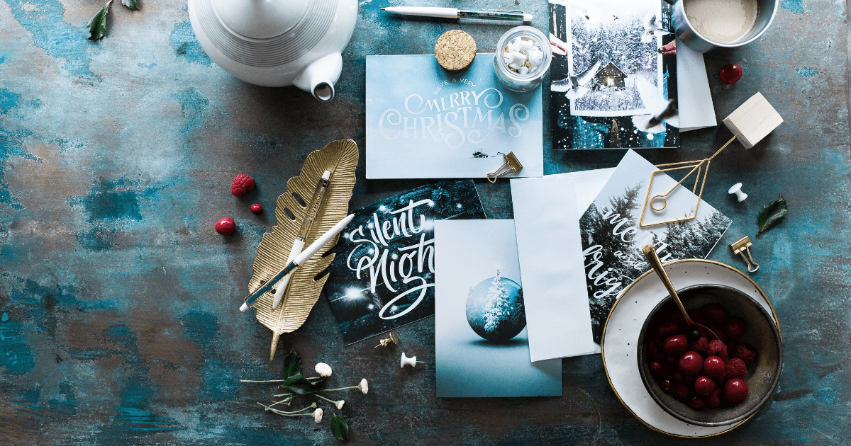 A table covered in assorted holiday items like cards, photos, tea, and gold coloured items