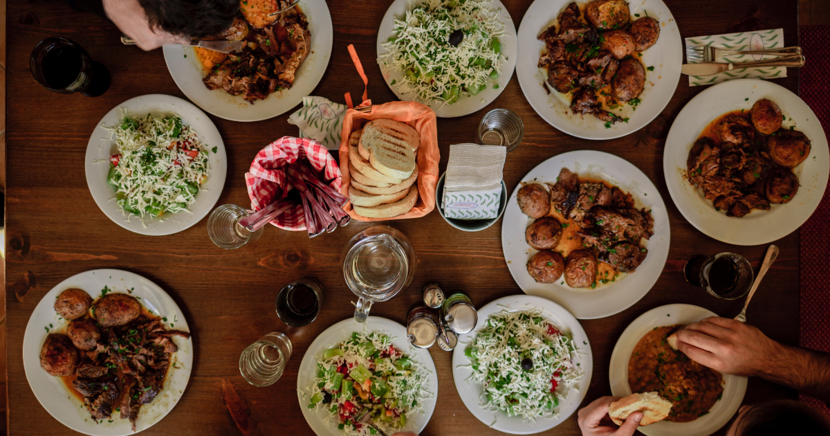 People eating at a dinner table off white dinner plates with assorted foods