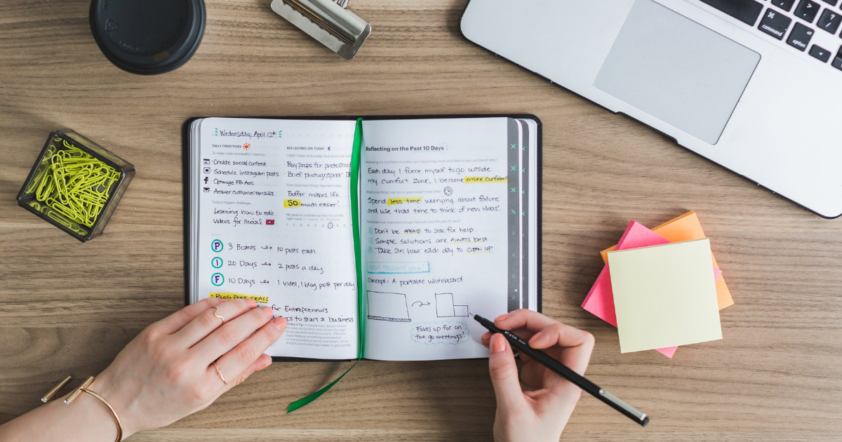 An open notebook on a desk surrounded by sticky notes and pencils