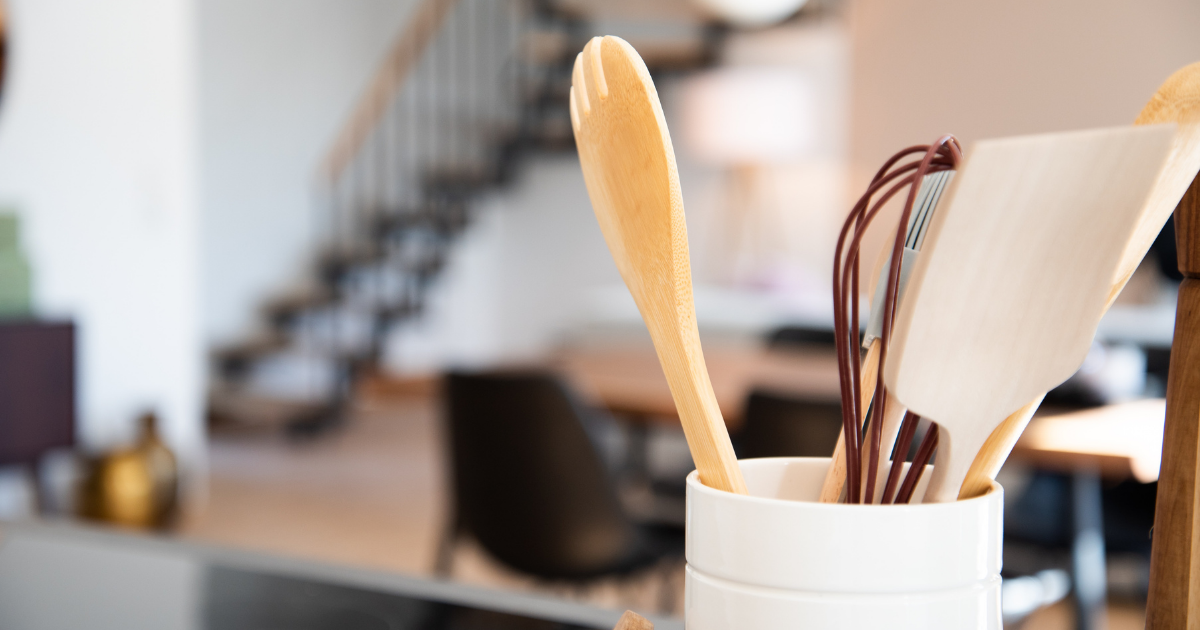 A jar sitting on a counter filled with wooden spoons, a wisk, and other baking supplies