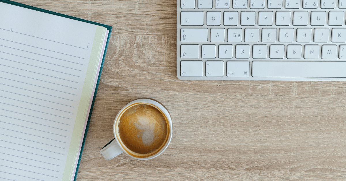 a coffe cup sitting on a desk near a computer and a notebook