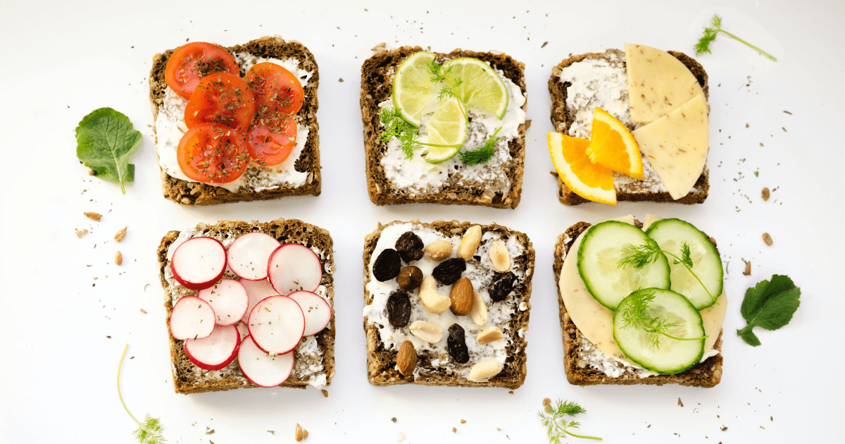 Pieces of toast topped with healthy toppings like avocado, tomato, and cheese on a white counter top