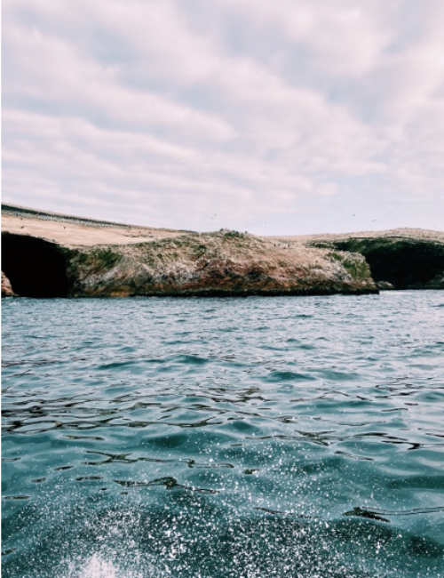 Waves splashing against a boat with rocks and a bright blue sky in the background