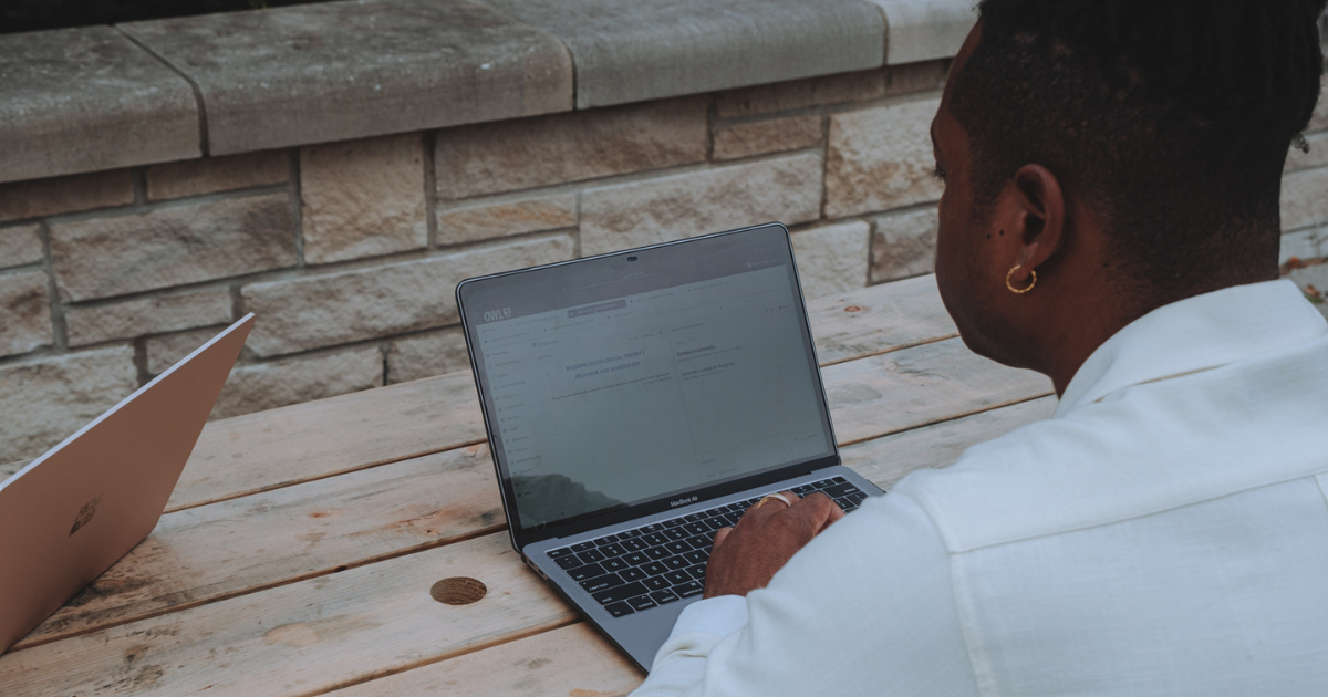 A person sitting at an ourdoor table studying on their laptop