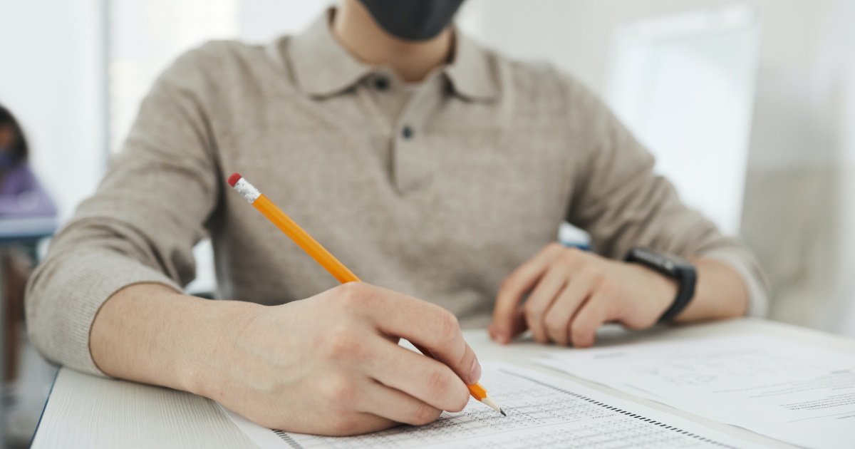 A student sitting at a desk in a classroom writing an exam with a scantron sheet