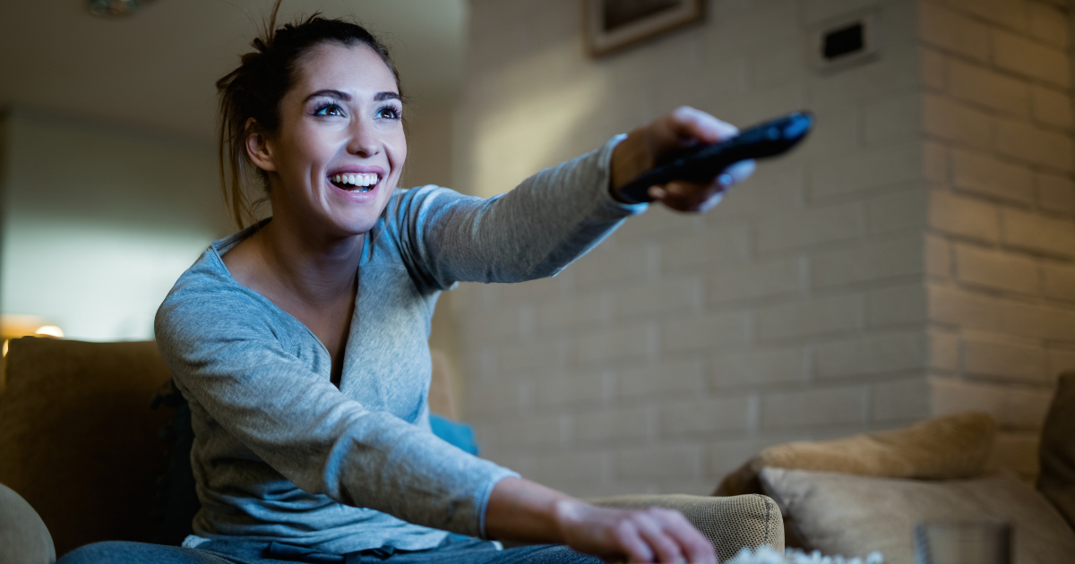 A person sitting on a couch with a bowl of popcorn getting ready to watch a movie