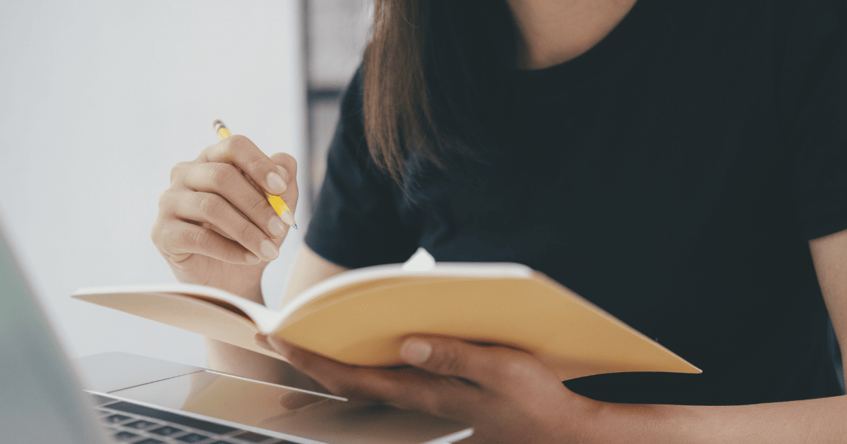 A person sitting at a desk with a laptop and a notebook studying