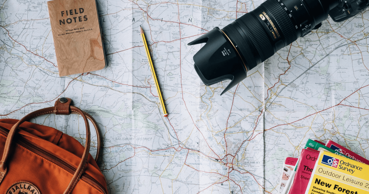 A backpack, camera, and notebook spread out on a map