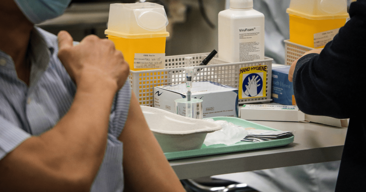 A person sitting with their sleeve rolled up waiting to receive a vaccine