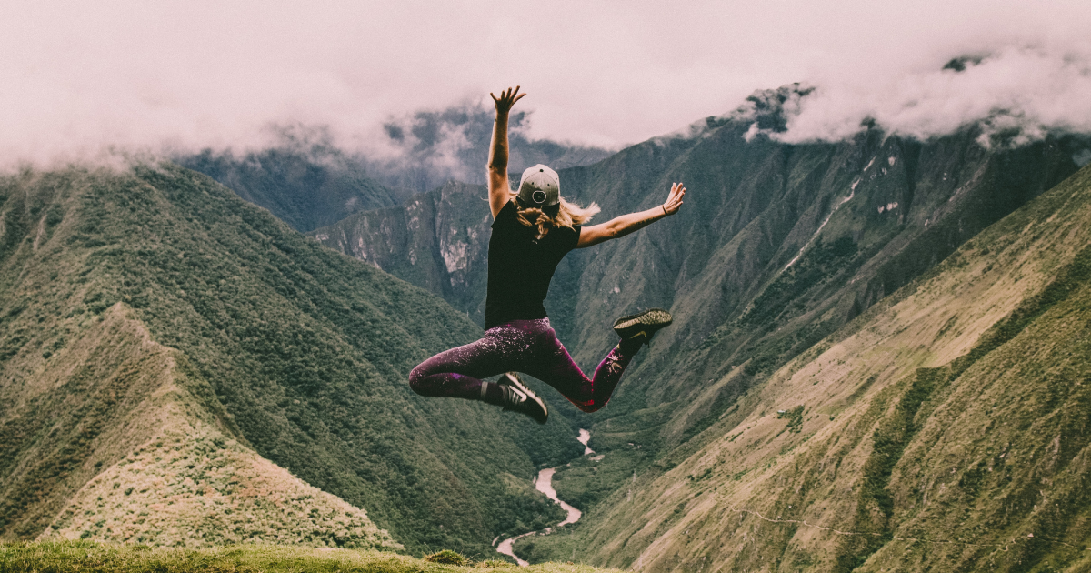 A photo of someone jumping with joy in front of a vast forrested area