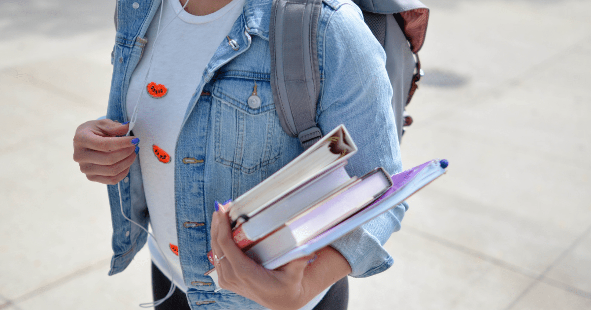 A person walking with a backpack on and carrying books and binders