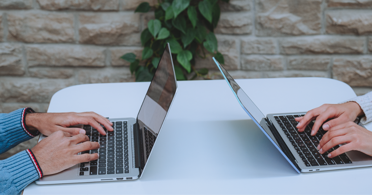 A photo of two people sitting at a table on their laptops