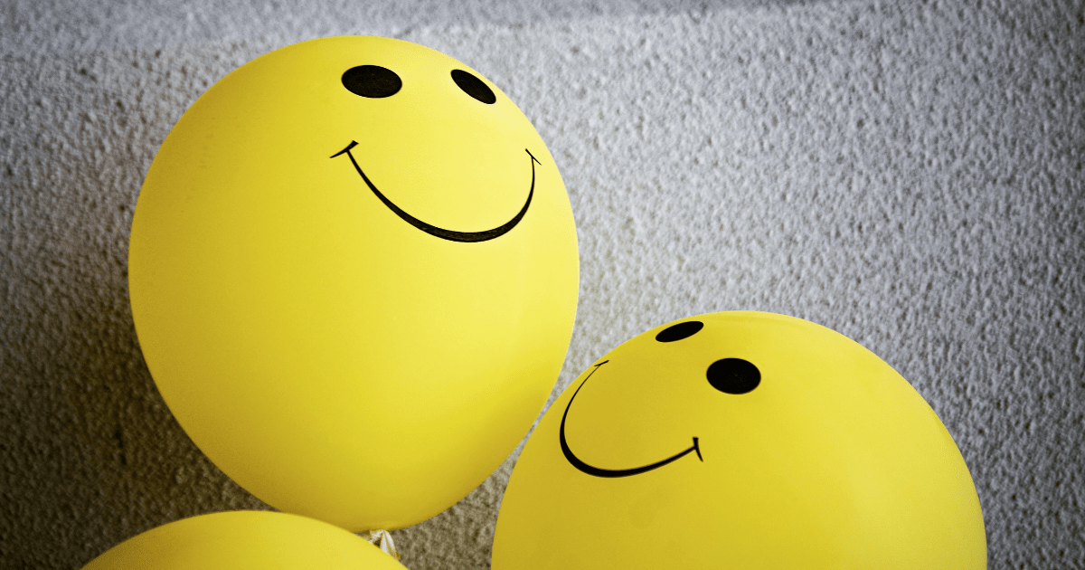 Yellow balloons with smile emojis on them against a grey wall