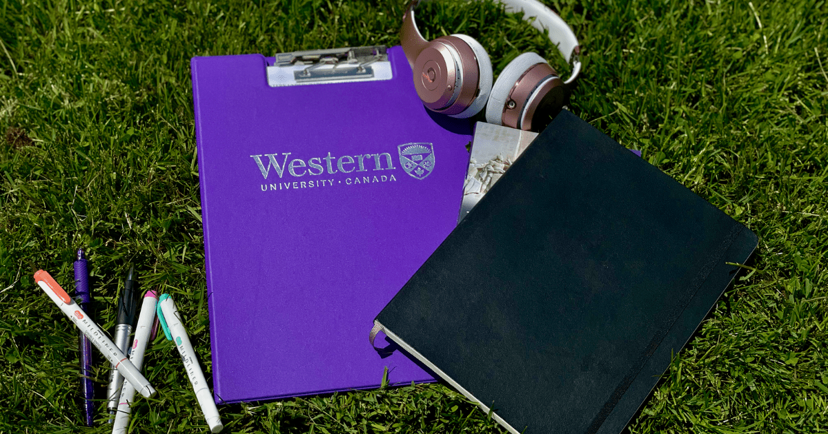 Pens, a Western notebook, and headphones laying in grass.
