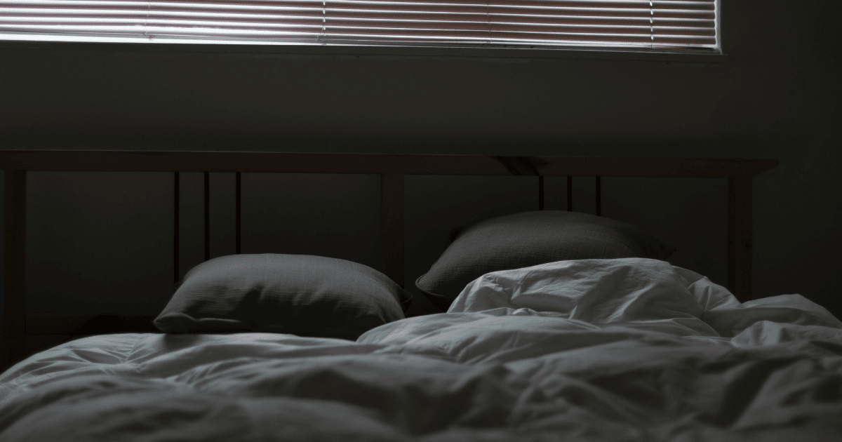 An image of an unmade bed in the dark