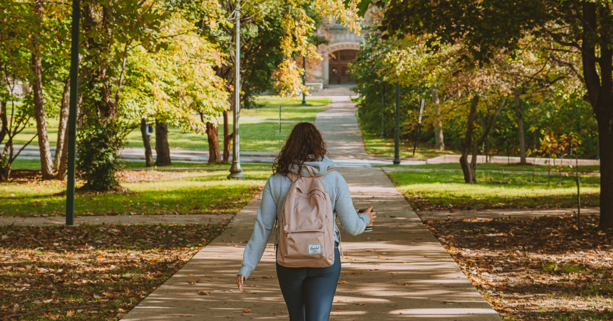 A student walking towards Middlesex College on campus surrounded by pretty fall trees