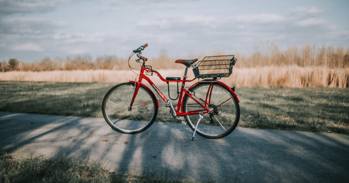 A bright red bike with a mesh basket standing on a sunny path