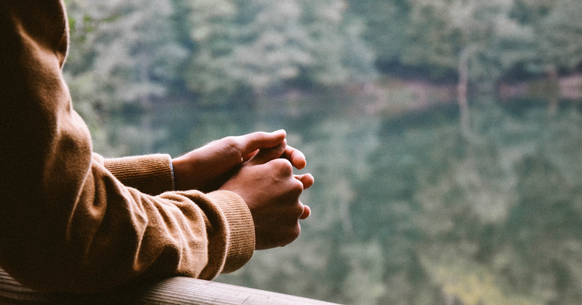 A person with their hands folded leaning over the edge of a railing