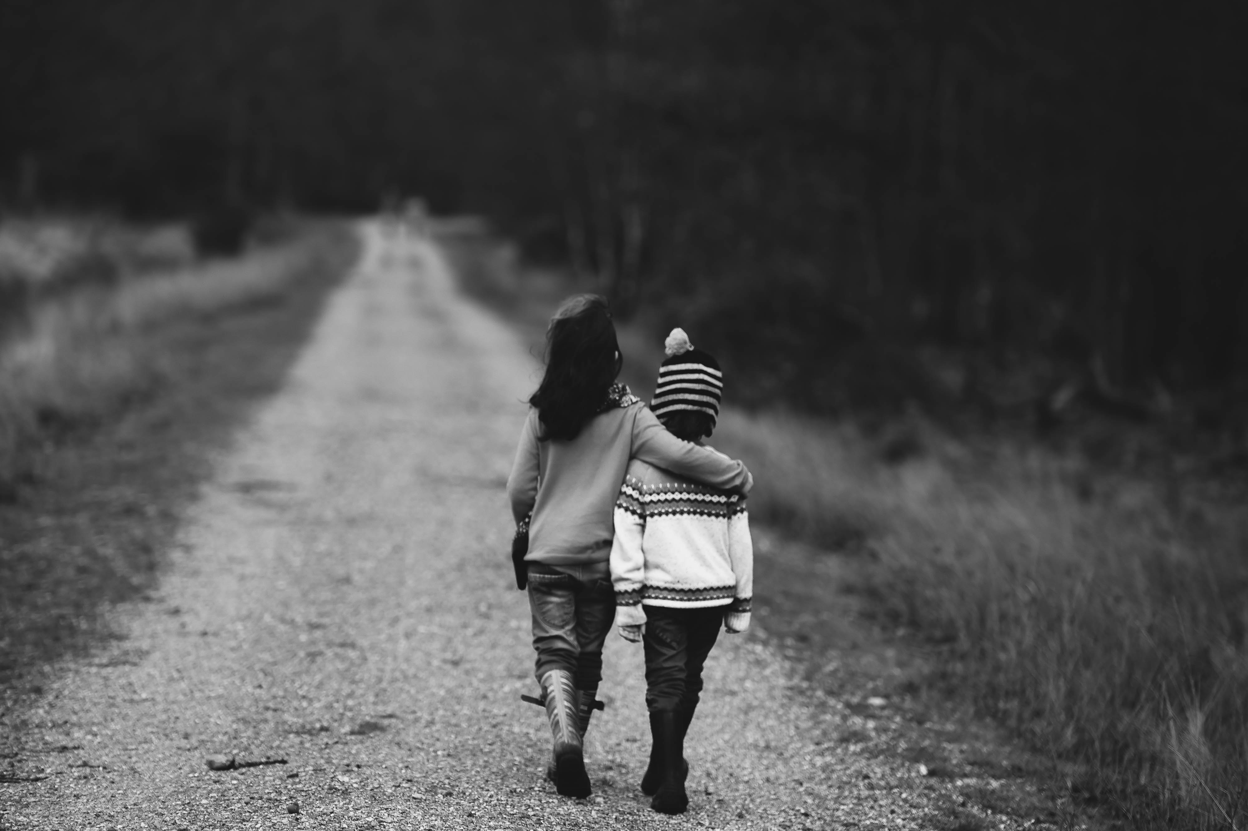 Two children walking with their arms around each other.