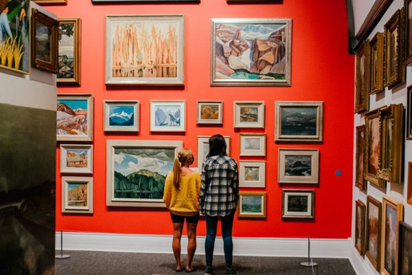 Two people looking at a wall of artwork in Museum London.