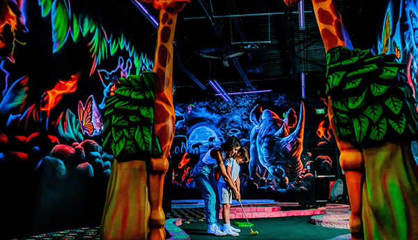 A mom teaching her son to mini golf at the indoor glow and the dark mini golf.