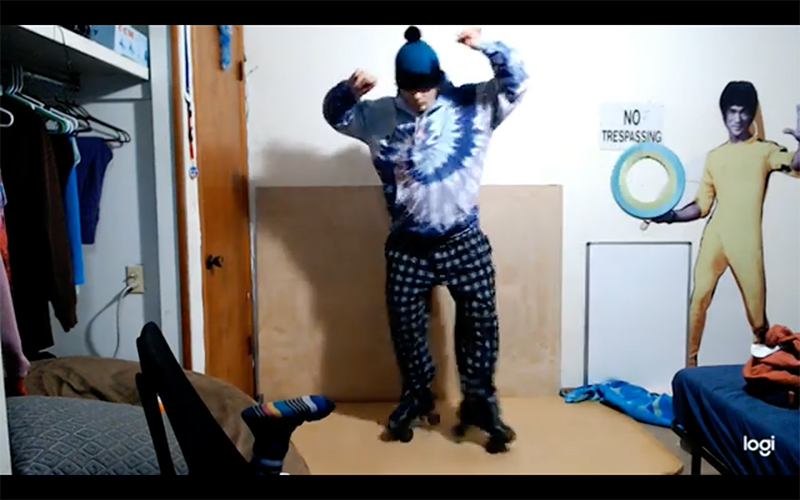 Video still of a person rollerblading in their apartment, a Bruce Lee cutout behind them