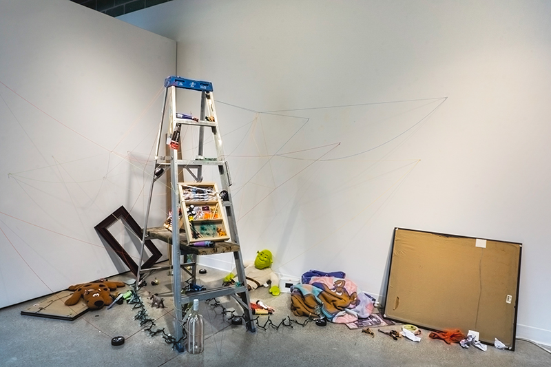 Photograph of an installation involving a ladder, thread, and personal belongings