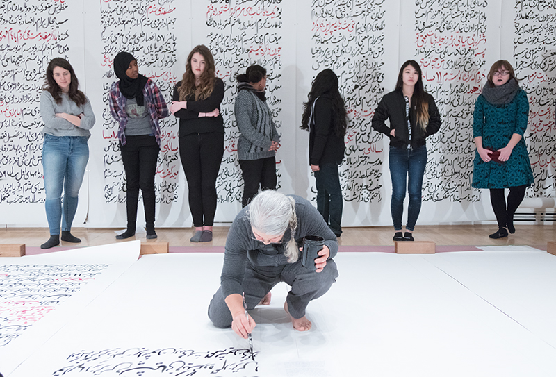 women standing in backgroud, artist croached in foreground working over paper