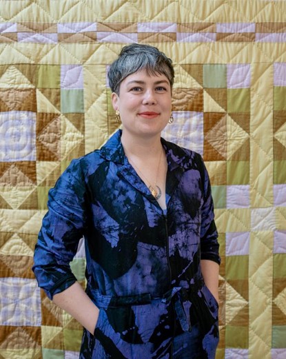 Image of artist Genevieve Flavelle standing in front of a colourful, geometric quilt