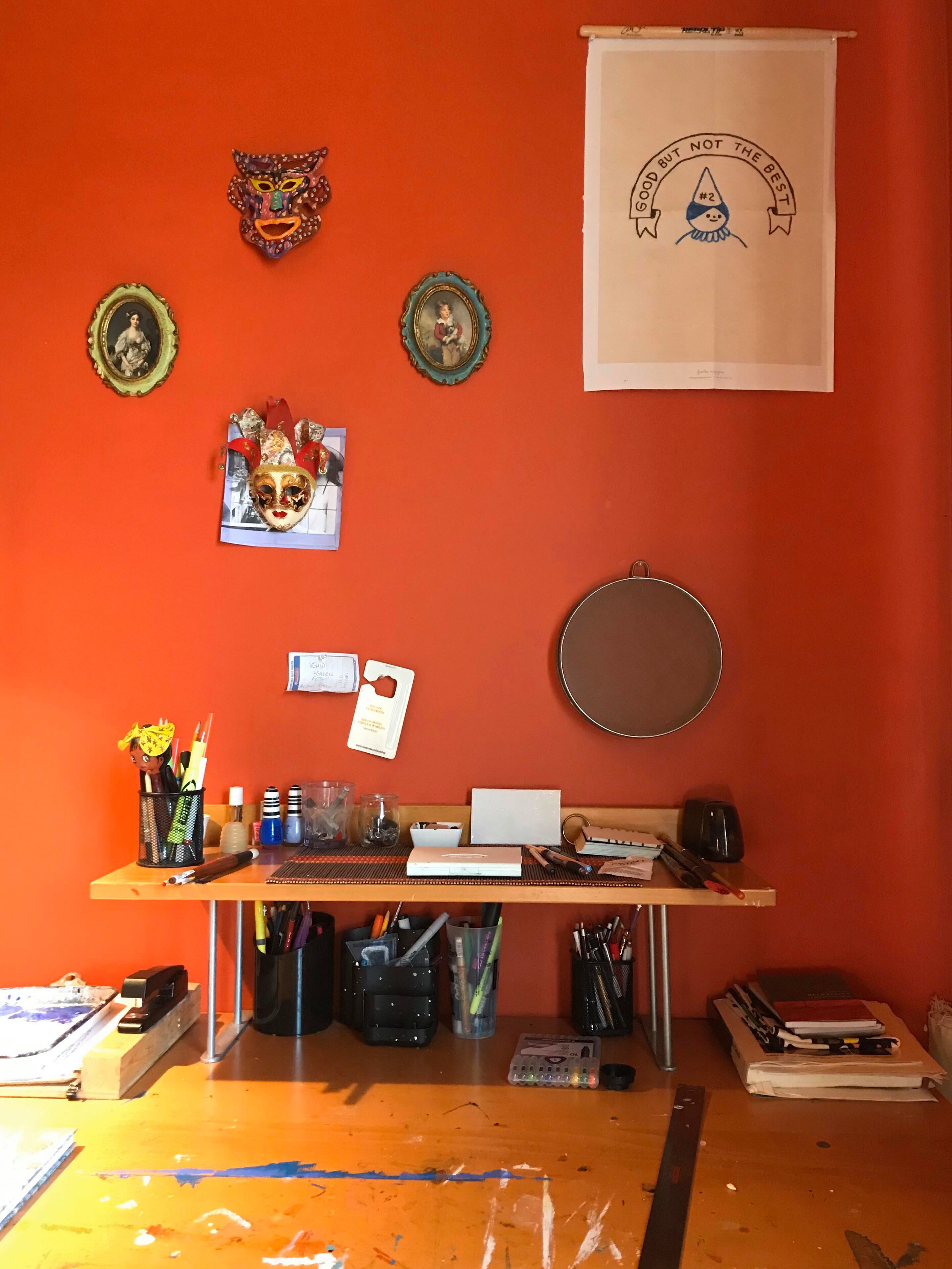Photo of an orange studio space with art and curios hanging on the wall above a desk.