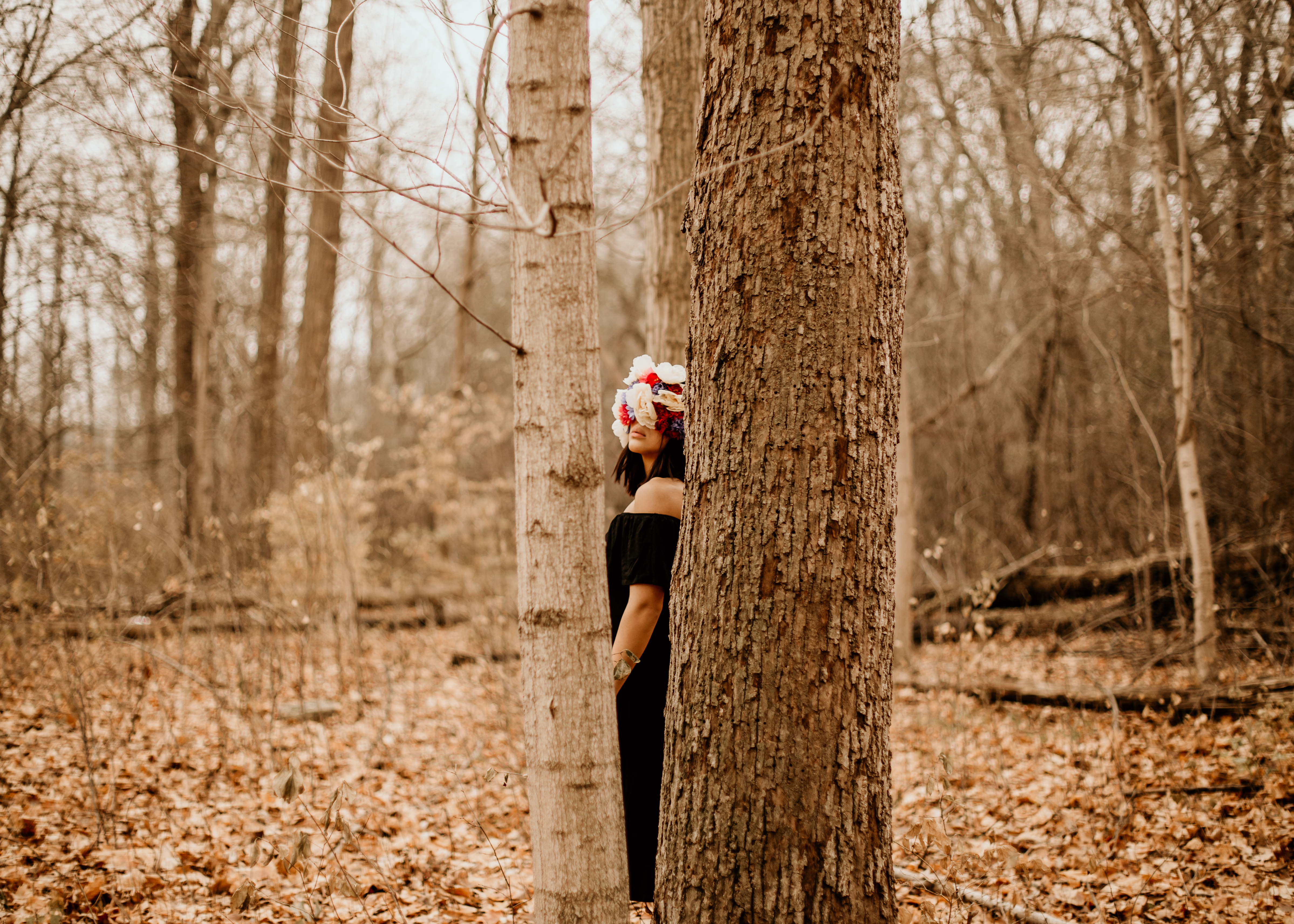 Photo of a woman standing between two trees with her face covered in white, red, and blue flowers.