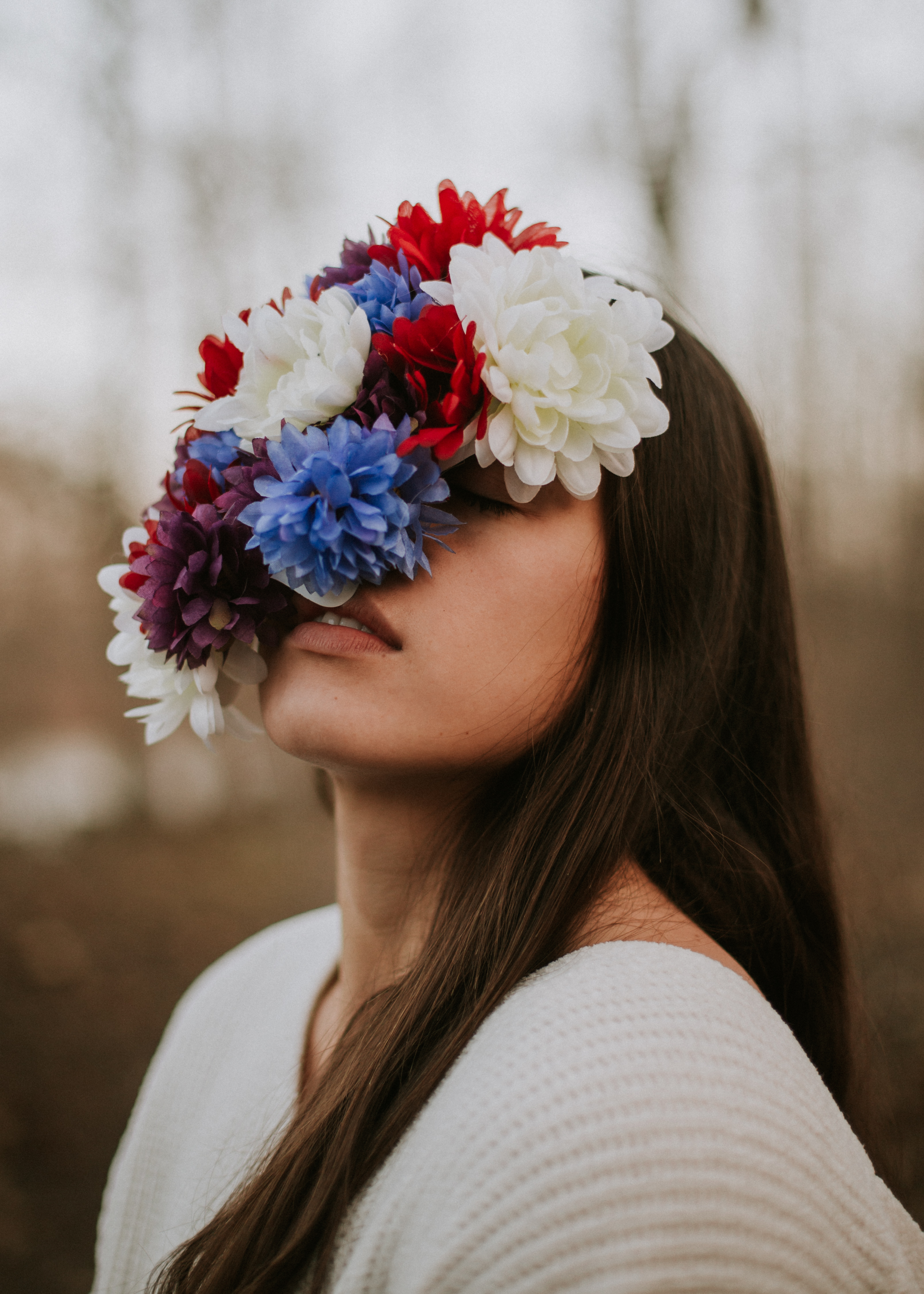 Photo of a woman wearing a white sweater with her face covered in white, red, and blue flowers.