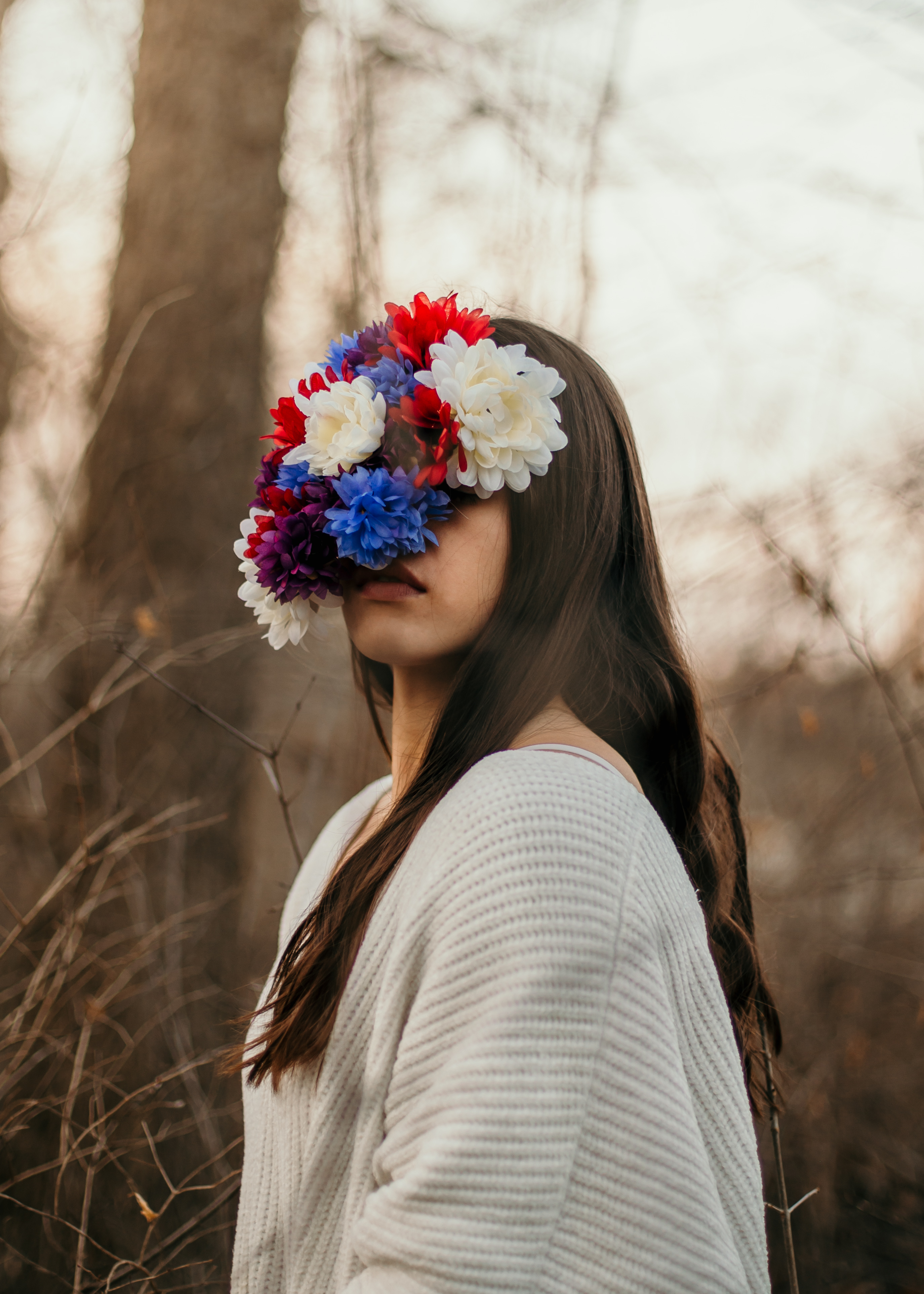 Photo of a woman wearing a white sweater with her face covered in white, red, and blue flowers.