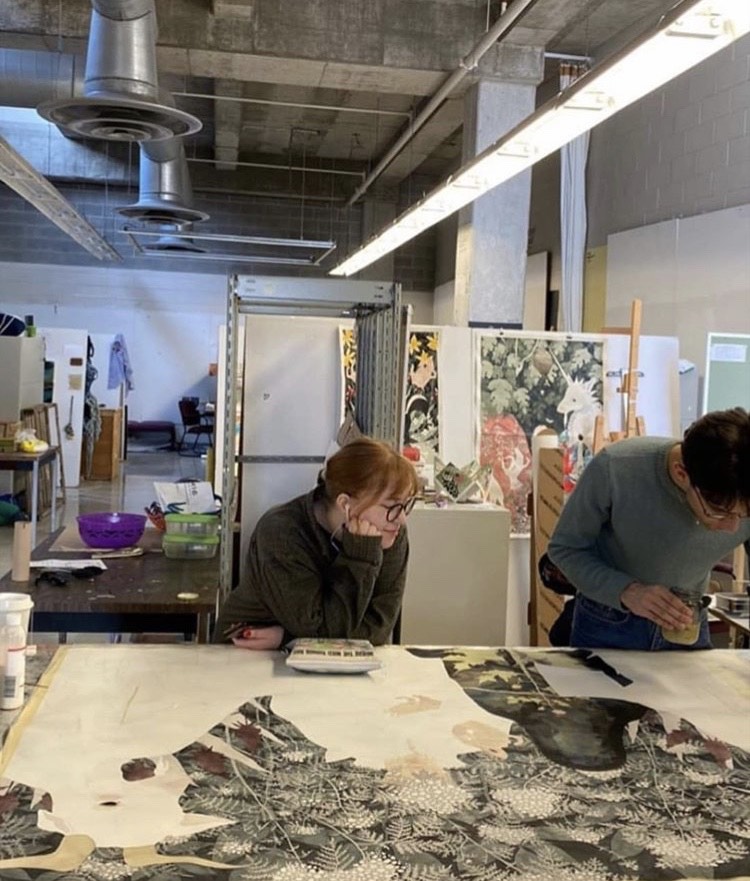 Photo of the artist working in their studio, standing over a large table.