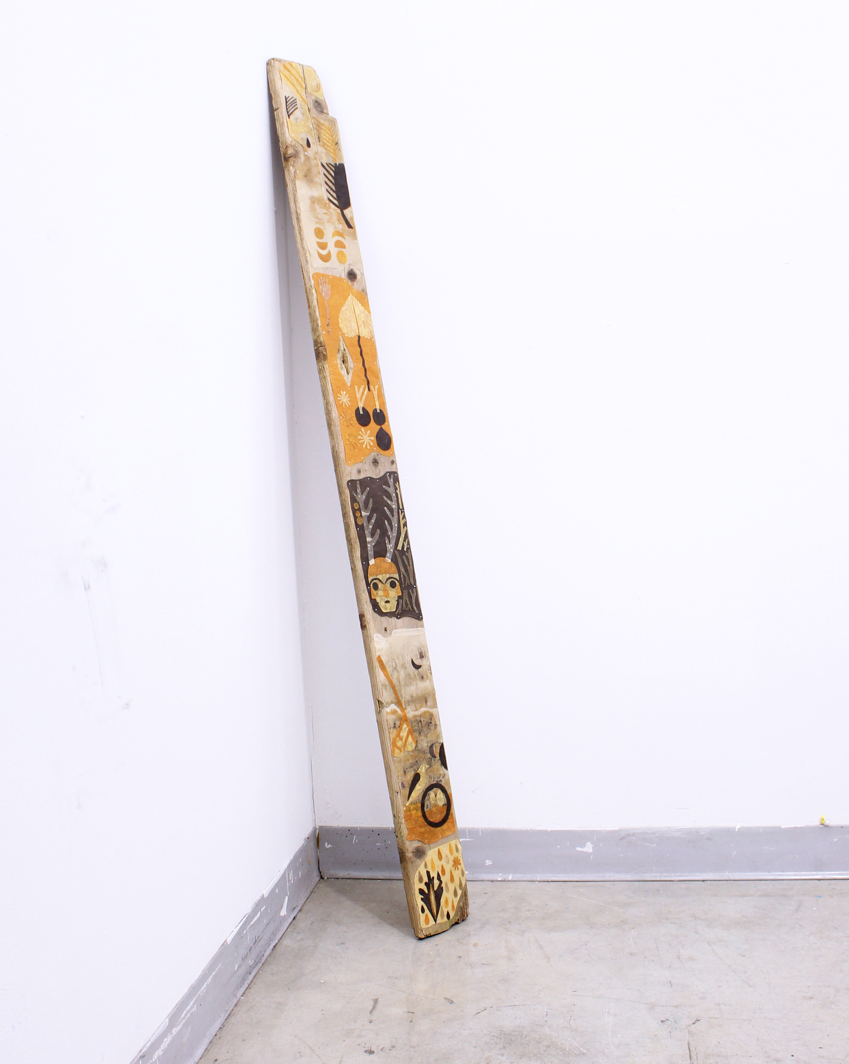 Plank of wood leaning against a white wall painted with yellow and brown organic shapes.