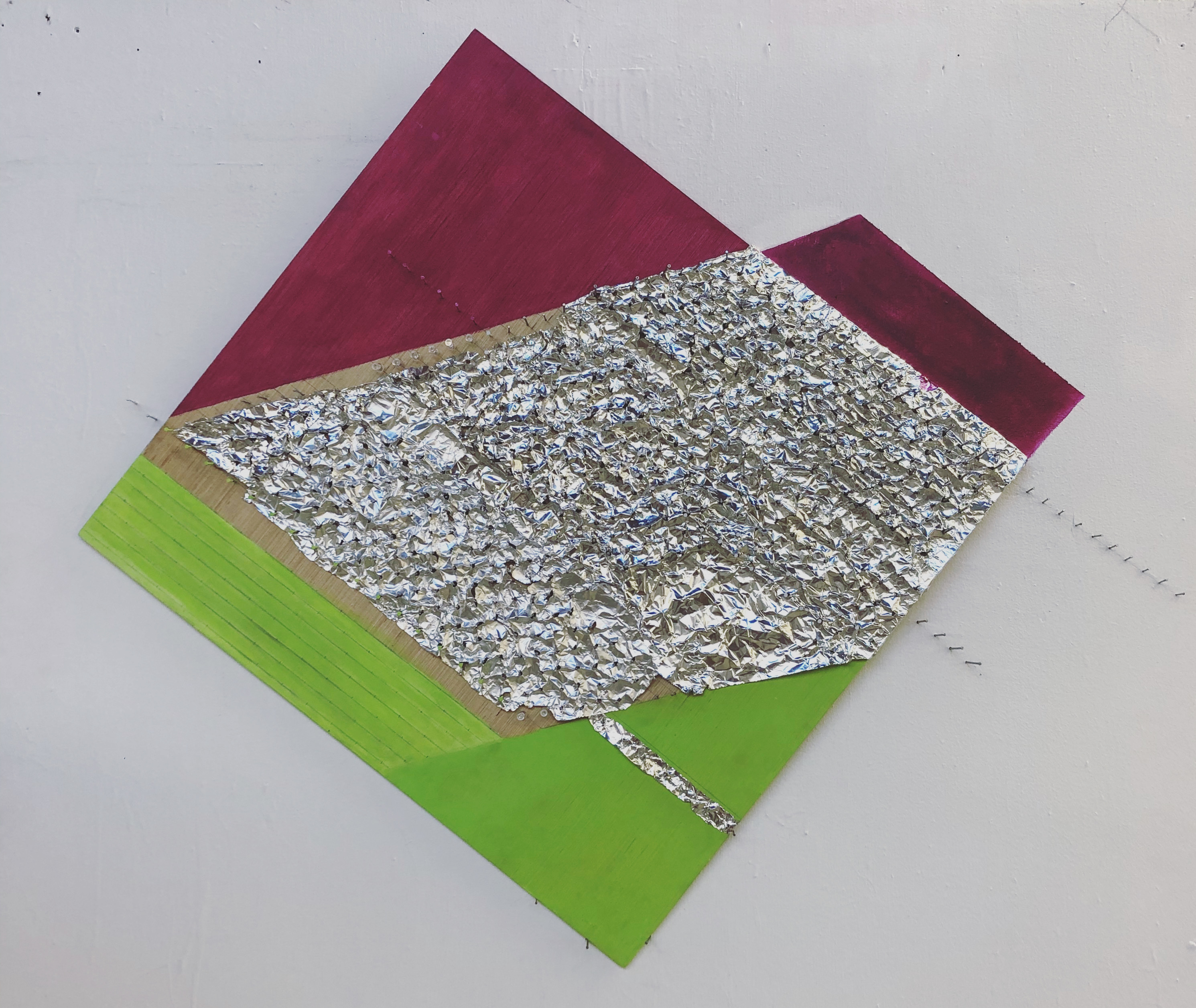 Photo of a panel affixed with foil paper and painted with red and green areas above and below the foil section.