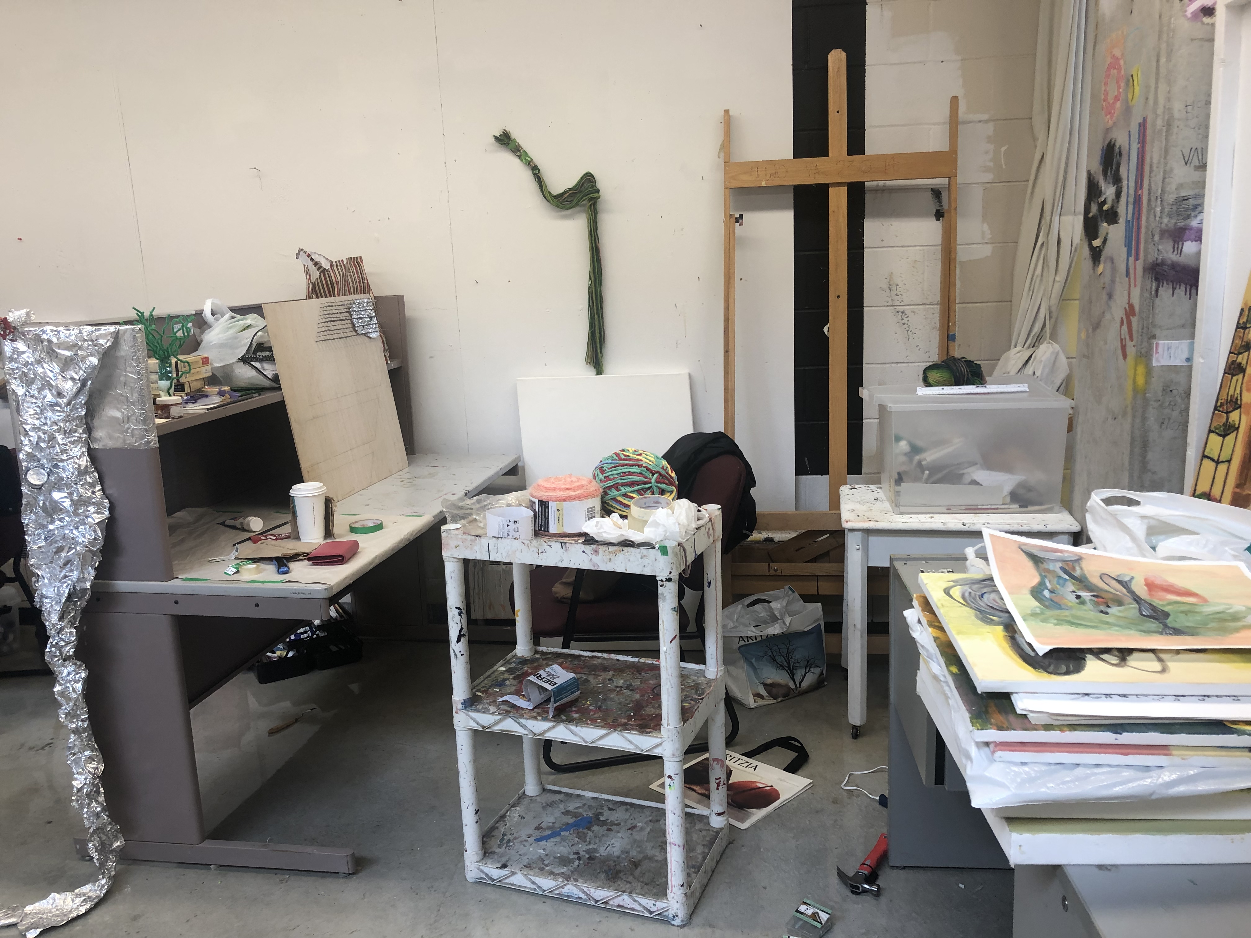 A photo of the artist's studio surrounded by prints, an easel, and other projects in situ.